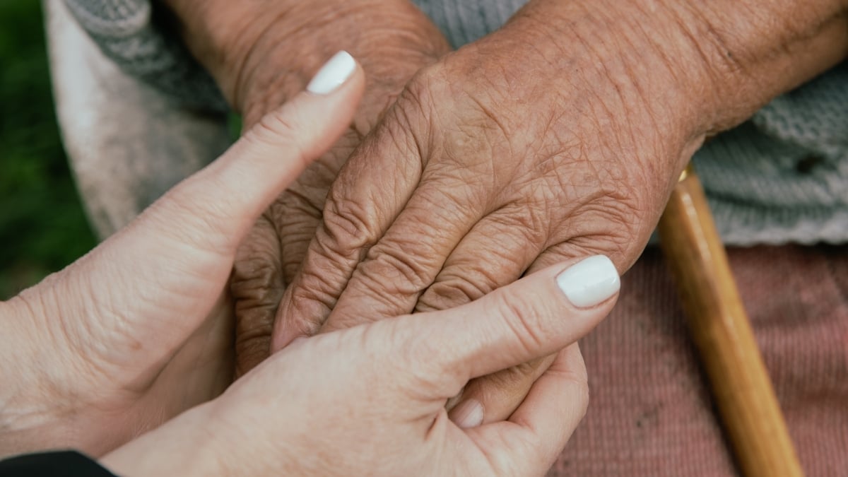 Caregivers hands holding an elderly person's hands.