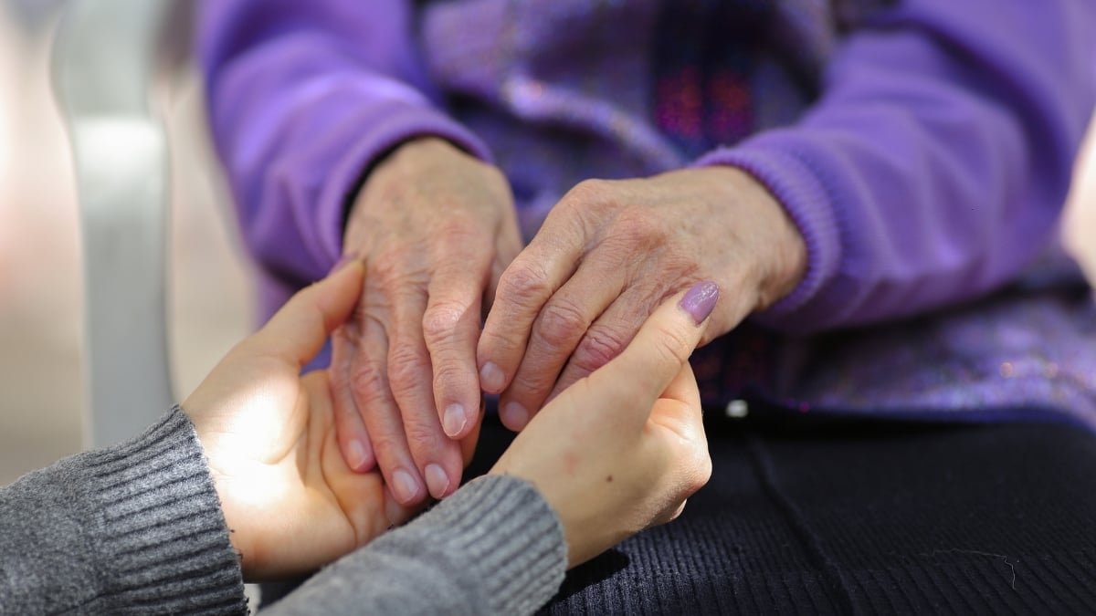 Caregiver holding senior woman's hands in hers.