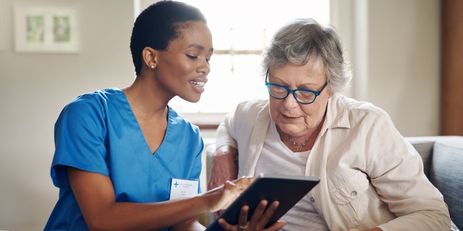 Smiling home health nurse showing an elderly patient information on a tablet.