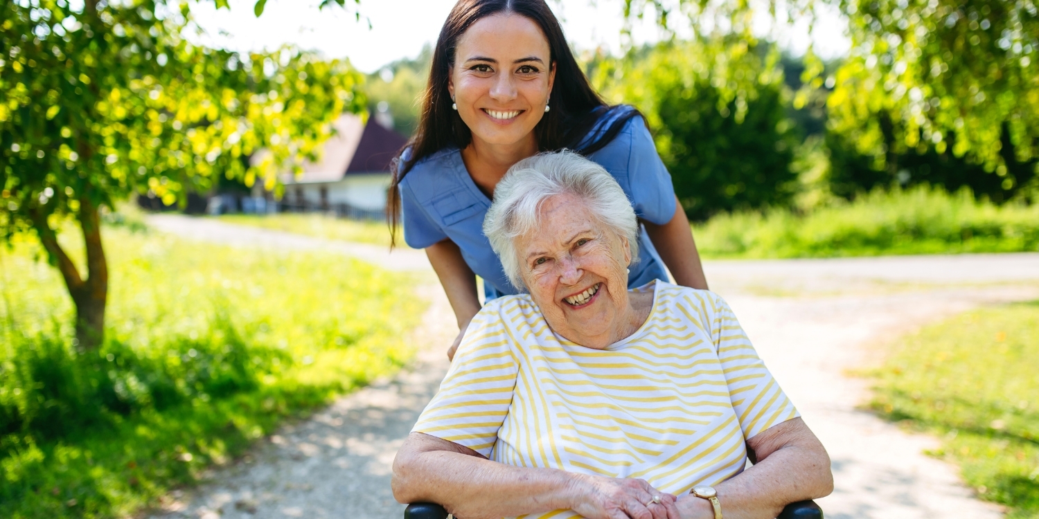 Home health nurse smiling outdoors with senior woman in wheelchair.