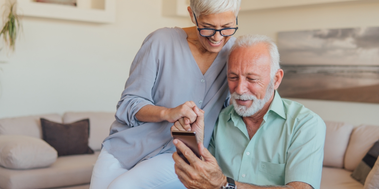 Senior couple sitting together smiling as they look at a smartphone