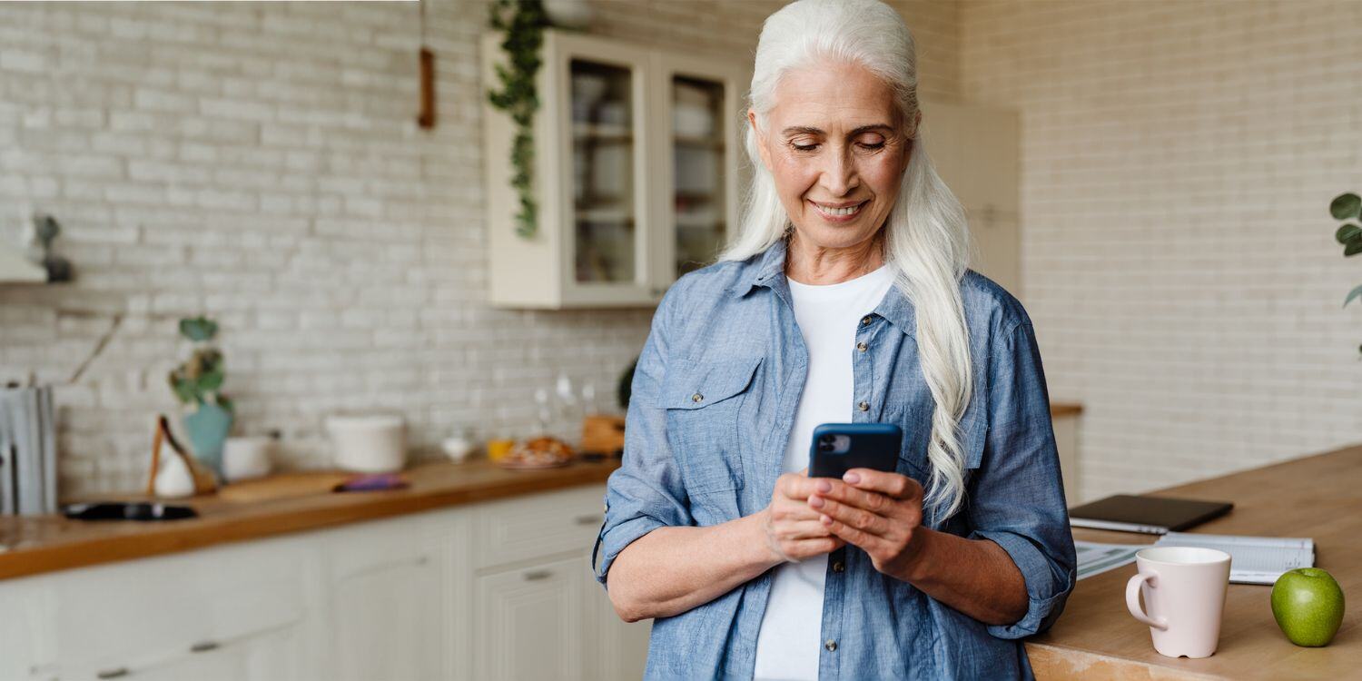 Senior woman smiling while texting on smartphone.