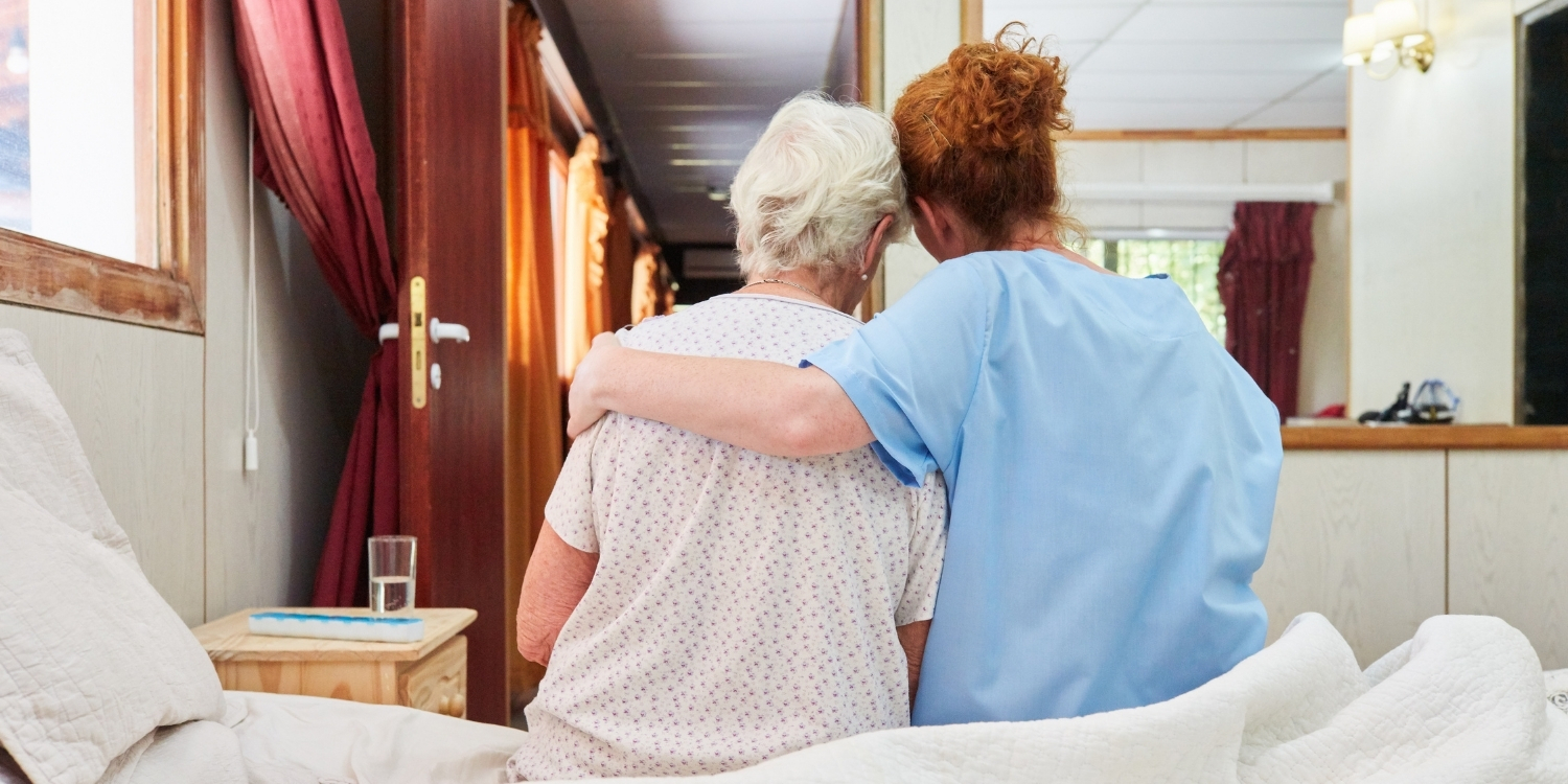 Clinician embracing an elderly patient at bedside.